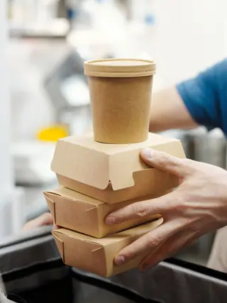 Kitchen worker holding a stack of cardboard takeaway food containers.